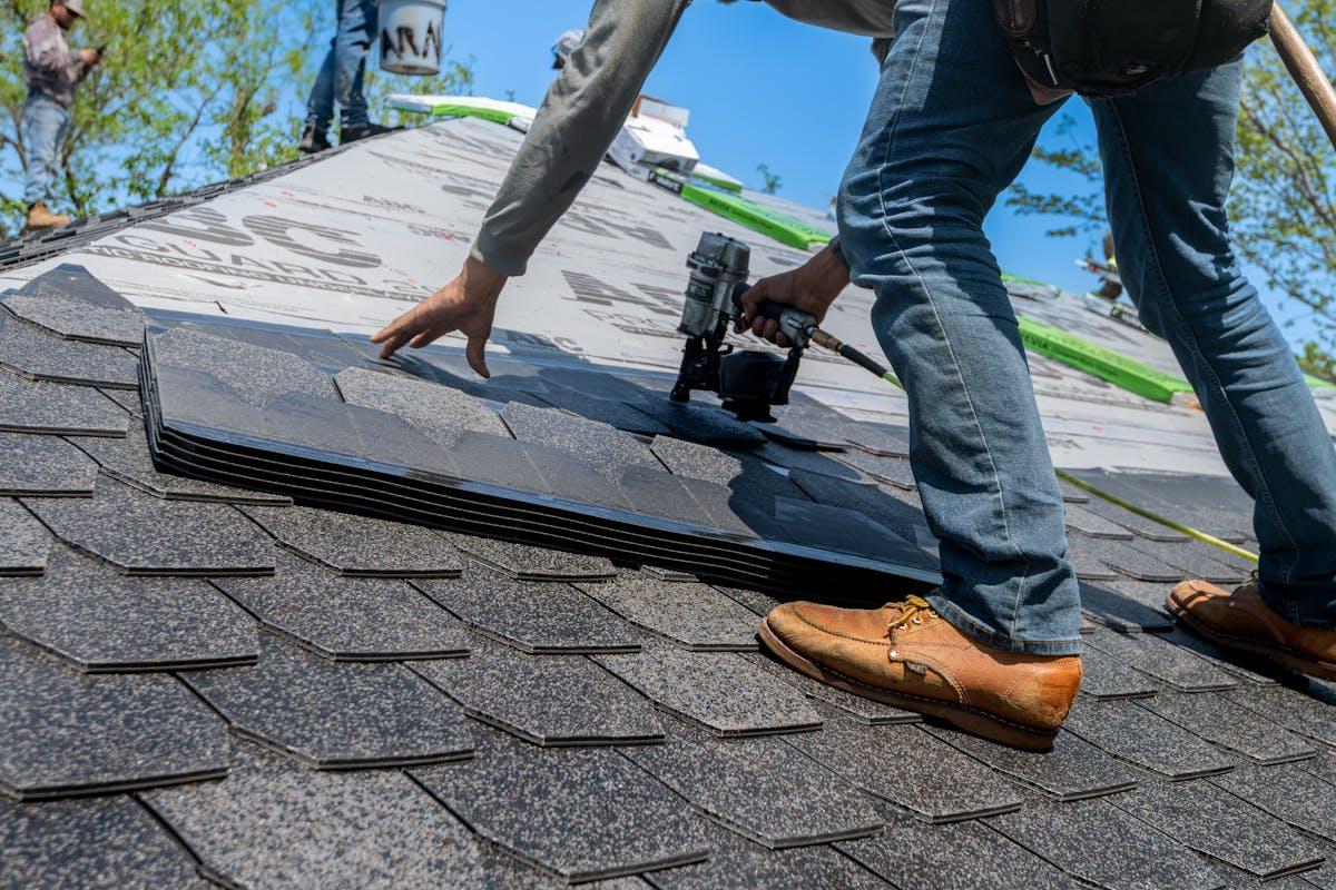 Roofer installing asphalt shingles with a nail gun